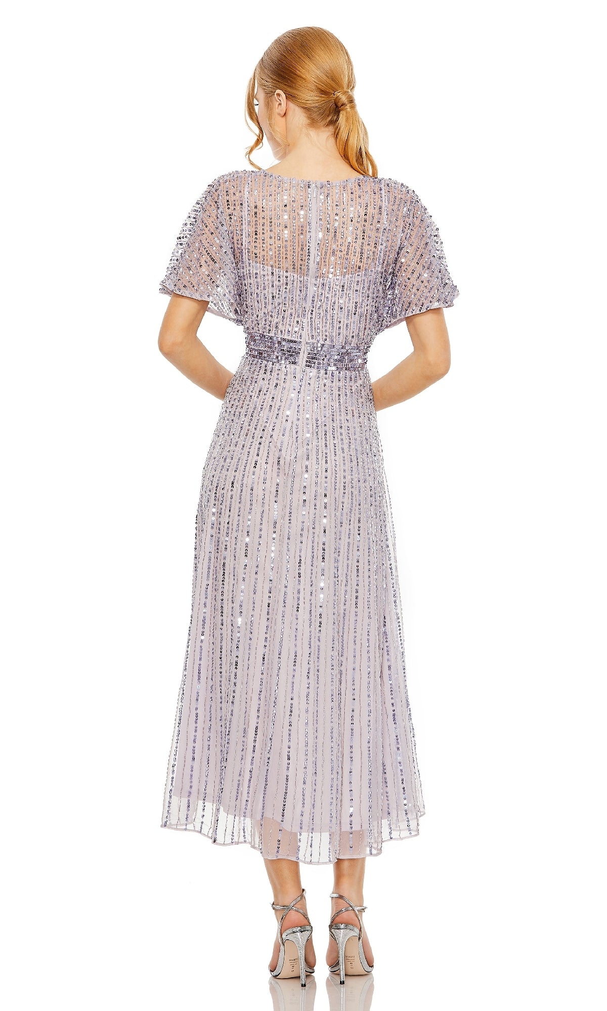 Woman stands with her back to the camera in the Mac Duggal 14007 Short Sequin Wedding-Guest Dress, a light purple, semi-formal style with vertical embellishments and silver heels—perfect for an elegant wedding guest look.